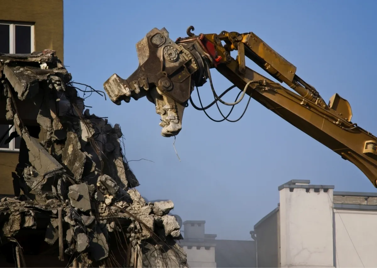 Demolition excavator claw tearing concrete from a collapsing building